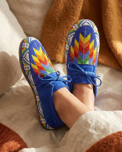 Hand-beaded royal blue moccasins with a rainbow flame and feather medallion edged in white beads