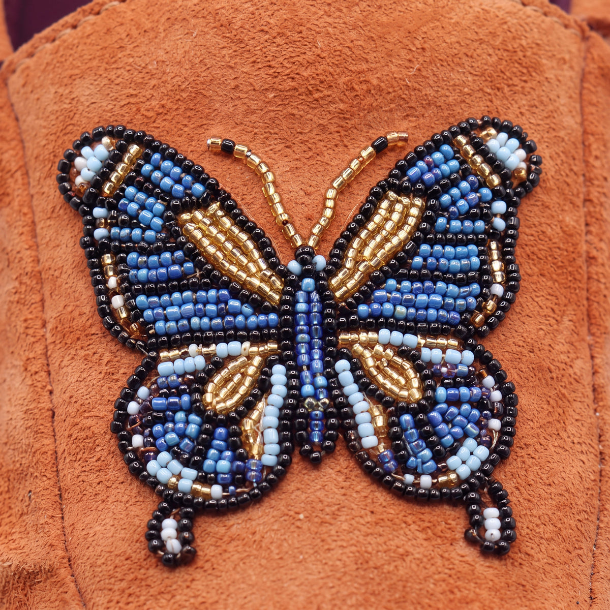 Close-up of blue, gold, black and white butterfly beadwork on coral suede moccasins