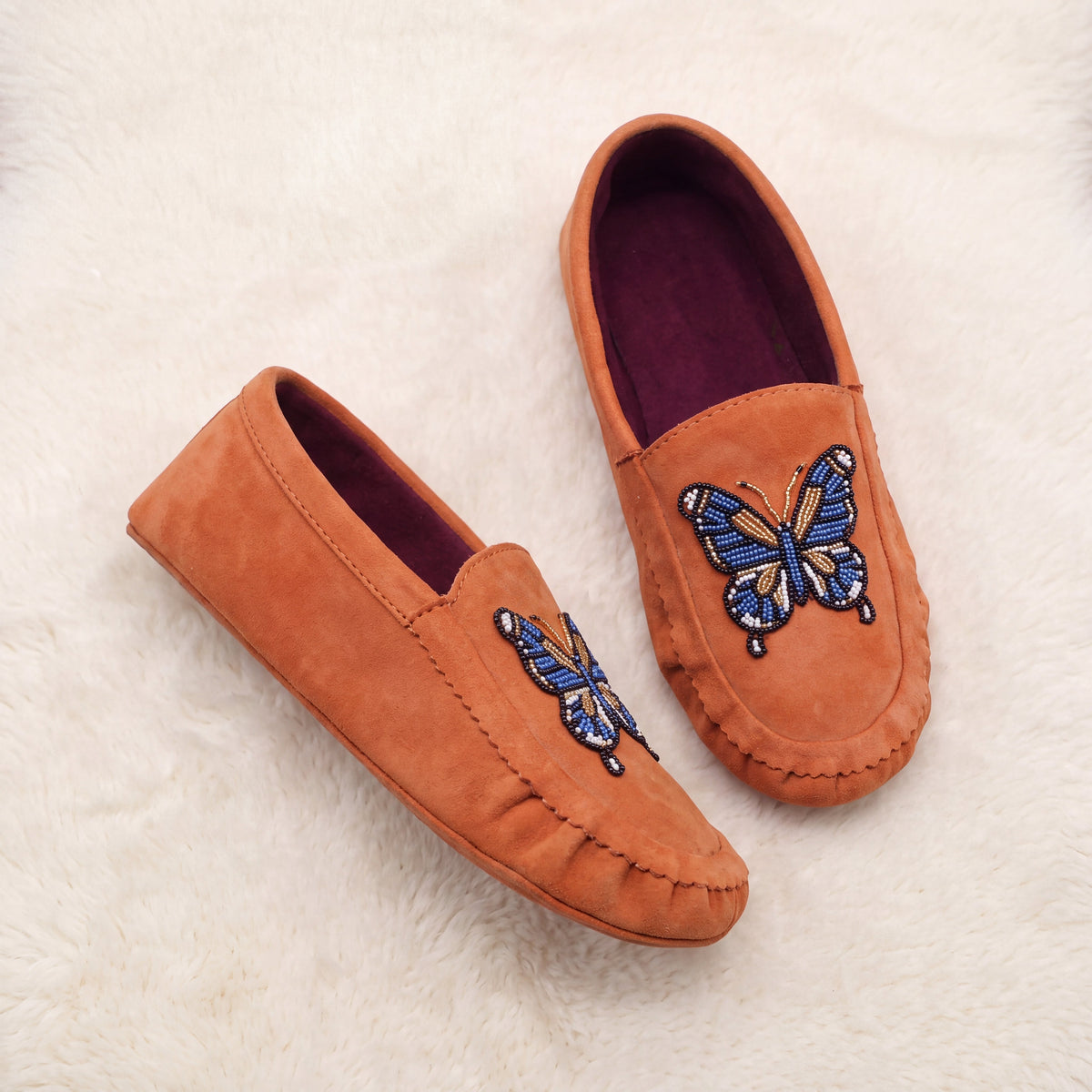Pair of women's coral suede butterfly beaded slip-on moccasins on warm ivory background