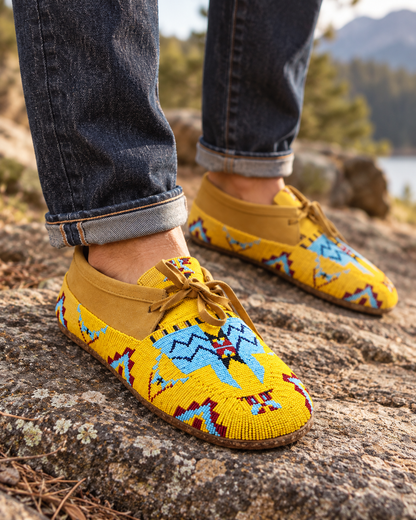 Man wearing yellow hand-beaded moccasins outdoors on rocky terrain